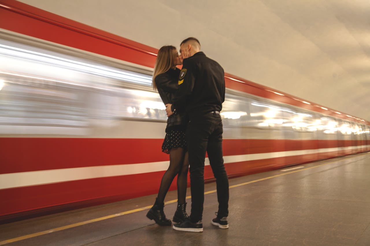 Side view of young stylish man and woman cuddling and kissing in subway near modern train in motion